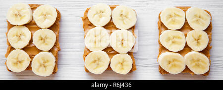 Vegan toasts avec beurre d'arachide et banane sur une surface en bois blanc, vue de dessus. Banque D'Images