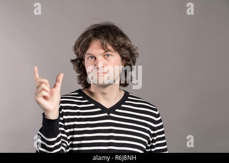 Hipster Young caucasian man wearing pullover rayé isolé sur fond gris, souriant et confiant des gestes avec la main faisant signe avec les doigts pendant la taille et à l'appareil photo. Mesurer le concept. Banque D'Images