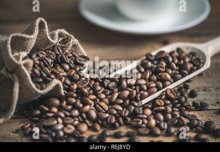 Les grains de café torréfié de sac de jute déversée sur fond de bois Banque D'Images