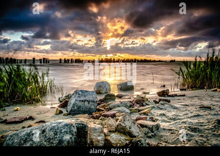 Coucher de soleil sur l'eau avec une vue sur l'IJsselmeer et orageux ciel nuageux. Rayons brillent à travers les tombes. de long temps d'obturation photographie avec fo Banque D'Images