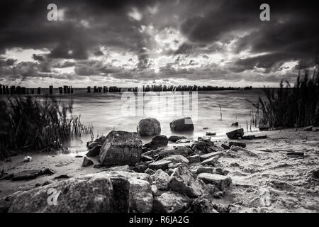 Coucher de soleil sur l'eau avec une vue sur l'IJsselmeer et orageux ciel nuageux. Rayons brillent à travers les tombes. de long temps d'obturation photographie avec fo Banque D'Images