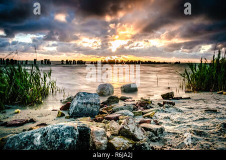 Coucher de soleil sur l'eau avec une vue sur l'IJsselmeer et orageux ciel nuageux. Rayons brillent à travers les tombes. de long temps d'obturation photographie avec fo Banque D'Images