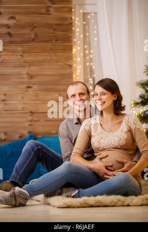 Photo de happy pregnant couple sur fond d'arbre de Noël décoré Banque D'Images