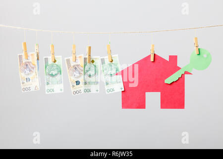 Maison Rouge avec touche verte et argent billets accrocher sur fil à linge sur fond gris. Vendre et acheter accueil concept. Banque D'Images