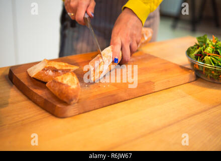 Cropped shot of woman cutting baguette de pain sur le dessus de table à la cuisine Banque D'Images