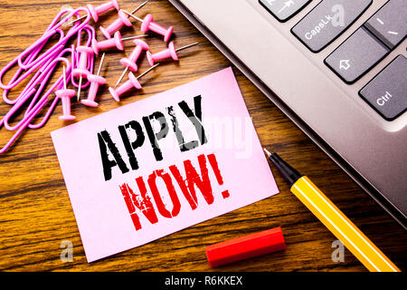 Texte manuscrit montrant Appliquer maintenant. Concept d'entreprise pour l'embauche d'emploi Application écrite sur papier rose post-it sur le fond de bois à côté du clavier. Avec stylo rouge. Banque D'Images
