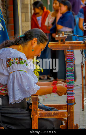 OTAVALO, ÉQUATEUR, 06 novembre 2018 : une femme non identifiée qui travaillent dans un bracelet fait main dans le trottoir à la ville d'Otavalo, Équateur. Banque D'Images