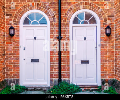 Deux portes avant d'habitation en bois blanc, avec un tuyau de vidange en bas du milieu. Les murs sont en brique rouge, il y a des arches lunette sur les portes métalliques et l Banque D'Images