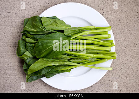 Choy sum (caixin) tiges et feuilles illustré sur les frais généraux d'une plaque blanche avec un fond en béton. Banque D'Images