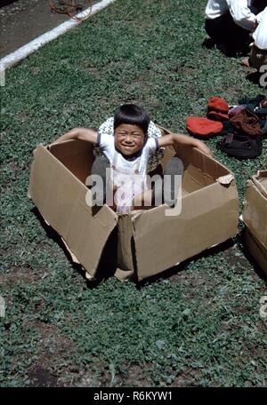 Photographie historique d'un jeune garçon japonais jouant dans un carton dans un champ au Japon, 1955. Banque D'Images