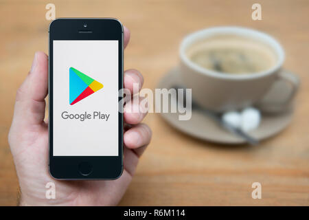 Un homme se penche sur son iPhone qui affiche le logo Google Play (usage éditorial uniquement). Banque D'Images