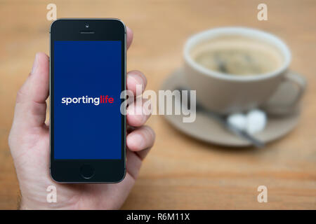 Un homme se penche sur son iPhone qui affiche le logo Vie Sportive (usage éditorial uniquement). Banque D'Images