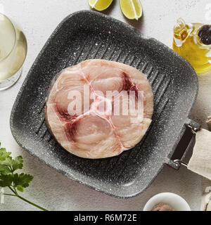 Steak d'espadon cru sur la poêle avec l'huile d'olive et les épices, de verre de vin blanc Banque D'Images