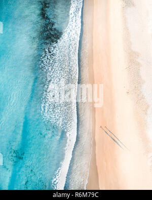 Vue aérienne de personnes marchant sur une plage au lever du soleil avec une belle plage de sable fin et de douces vagues Banque D'Images