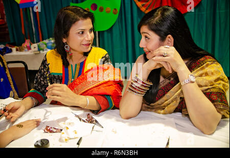 Deux femmes indiennes parler lors de l'application d'une conception traditionnelle avec un henna mehndi cône au Festival Internationational Mobile à Mobile, Alabama. Banque D'Images
