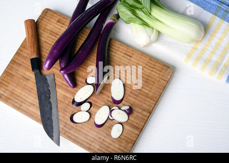 Aubergine japonaise sur planche de bois avec couteau et salade de pak choi Banque D'Images