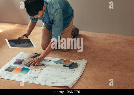 Man holding digital tablet sur étage avec plan de logement et des couleurs du nuancier. La sélection Designer couleurs pour nouveau projet de maison. Banque D'Images