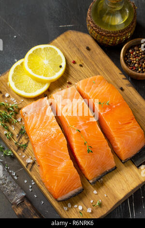 Le poisson frais. Filet de saumon cru, de citron et d'épices sur une planche en bois rustique sur une table en pierre. Banque D'Images
