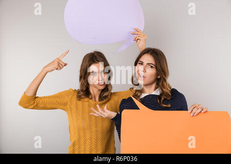 Image de deux jolies femmes smiling and holding banner with copyspace isolé pour le texte sur fond gris Banque D'Images