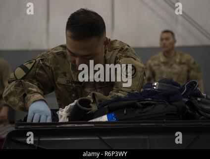 La CPS de l'armée américaine. Jong Wook Shin, 368e Compagnie de Police Militaire, inspecte le contenu d'une pièce de bagage à l'aérodrome de Bagram, en Afghanistan, le 30 avril 2017. Au cours de leurs inspections, l'équipe des douanes suit des lignes directrices rigoureuses de plusieurs agences gouvernementales, pour inclure le U.S. Customs and Border Protection, Ministère de l'Agriculture des États-Unis et le Bureau of Alcohol, Tobacco, Firearms and Explosives lors d'une recherche dans les bagages. Banque D'Images