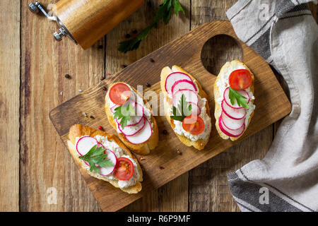 Antipasti des collations pour le vin. Brushetta ou Crostini avec baguette grillées, fromage, radis et tomates sur une table en bois. Vue supérieure de la télévision mise de fond. Banque D'Images