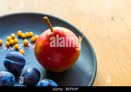 Still Life - prunes juteuses, grand bleu, de poire mûre et de petits fruits de l'argousier dans une plaque en céramique sur un fond de bois, close-up Banque D'Images