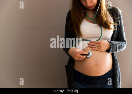 L'écoute de la femme enceinte à son bébé dans le ventre avec un stéthoscope Banque D'Images