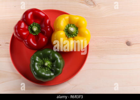 Trois poivrons doux dans une plaque rouge sur un fond de table en bois Banque D'Images