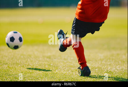 Young Football Player Kicking Ball sur le terrain de soccer. Boy Wearing Red Sports Jersey, short noir, chaussettes football Rouge et Noir tasseaux. Kick Soccer sur Banque D'Images