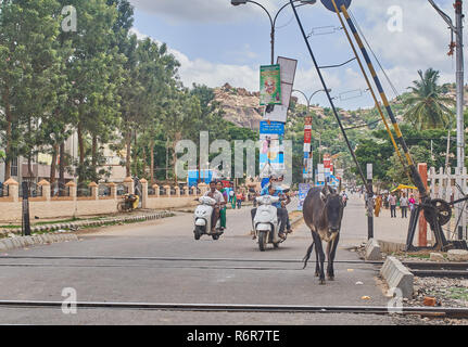 Une vache et quelques scooters de la conduite sur une voie ferrée dans l'Inde du sud pendant une chaude journée d'été. Banque D'Images