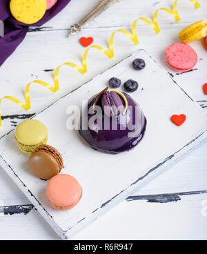 Gâteau rond lilas avec des macarons sur une planche de bois blanc Banque D'Images