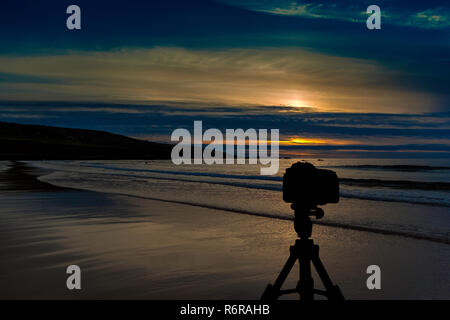 Appareil photo sur trépied avec coucher de soleil sur l'océan en arrière-plan Banque D'Images