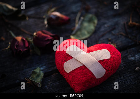 Bande de premiers soins médicaux de la bande de plâtre rembourré collés sur Patch coeur rouge séché avec rose rouge sur fond de bois. Coeur brisé, l'amour et la notion de Jour de Valentines. Banque D'Images