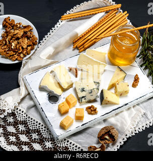 Différents morceaux de fromage sur une planche de bois blanc près d'un pot de miel Banque D'Images