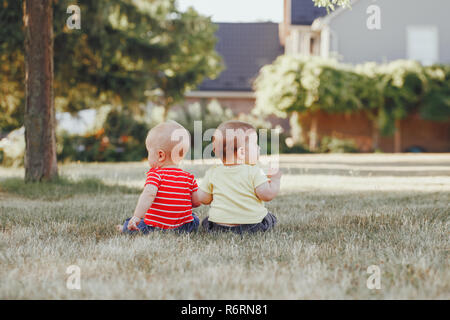 Deux adorables petits bébés blancs assis ensemble dans le champ extérieur prairie à différentes façons. Vue de derrière. Dans Cchildren parc d'été. Banque D'Images