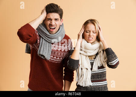 Portrait d'une jeune couple vêtus de pulls et tricots ensemble permanent fond beige plus isolés, ayant un mal de tête Banque D'Images