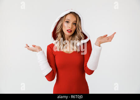 Portrait d'une femme blonde perplexe habillés en costume de Nouvel An rouge isolés sur fond blanc, haussant les épaules Banque D'Images