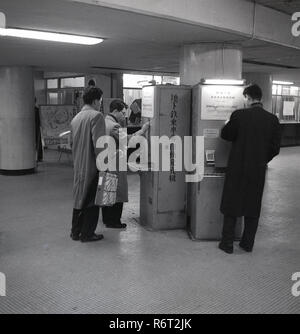 Années 1960, historique, les hommes japonais banlieusards obtenir les tickets de métro à partir de distributeurs automatiques dans le hall sur le métro de Tokyo. Banque D'Images