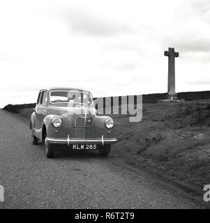 Années 1950, historiques, une automobile de l'époque en stationnement sur une route sur une colline, à côté d'une croix de pierre, de l'Irlande Banque D'Images