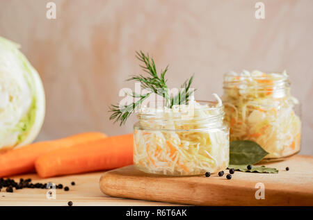 Les bocaux en verre avec choucroute et ingrédients pour sa préparation : le chou et les carottes sur fond clair. Banque D'Images