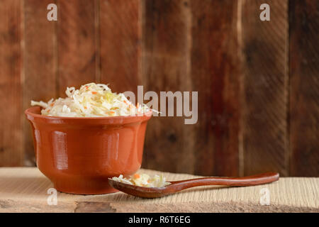 Brown clay pot et cuillère en bois avec la choucroute sont debout sur planche de bois contre le mur en bois. Banque D'Images