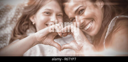 Mère et fille faisant la forme du coeur avec les mains tout en étant couché sur le lit Banque D'Images