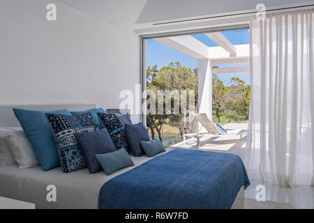 Coussins assortis dans des tons de bleu sur un lit double avec vue sur la terrasse de la piscine dans villa de nouvelle construction, Quinta do Lago Banque D'Images