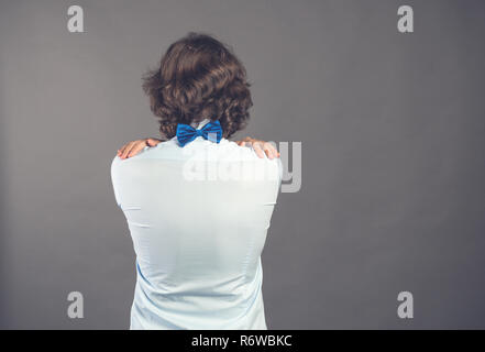 Jeune homme en chemise bleu et dentelle épouse lui-même sur fond gris. Vue arrière. Ses mains se trouvent sur l'arrière. Il a besoin d'être embrassé. Sentiment égoïste, l'amour vous-même concept. Les émotions positives. Copy space Banque D'Images