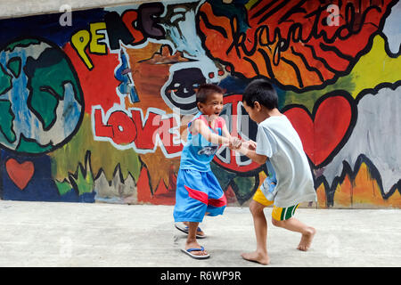 Les enfants de la rue enfants tournent en face d'un mur de graffiti à l'Kuya Center pour les enfants de la rue à Quezon City, Metro Manila, Philippines. Banque D'Images