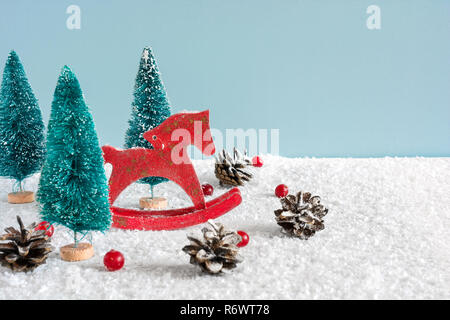 Cheval jouet rétro Noël avec sapins, fruits rouges et des pommes de pin sur table en bois couverte de neige sur fond bleu. Noël ou bonne ye Banque D'Images