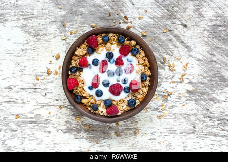 Bol de céréales d'avoine avec du yogourt, des framboises, bleuets et les écrous sur la table en bois blanc, pour un petit-déjeuner sain, vue d'en haut Banque D'Images