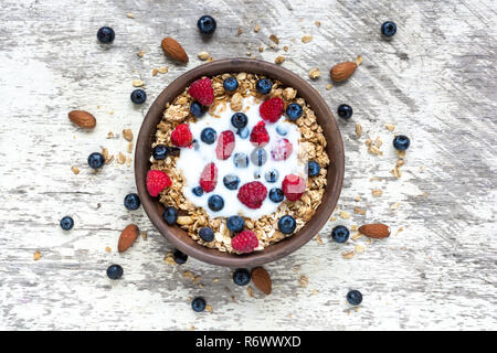 Bol de céréales d'avoine avec du yaourt grec, framboises, bleuets et les écrous sur la table en bois blanc, pour un petit-déjeuner sain, vue d'en haut Banque D'Images