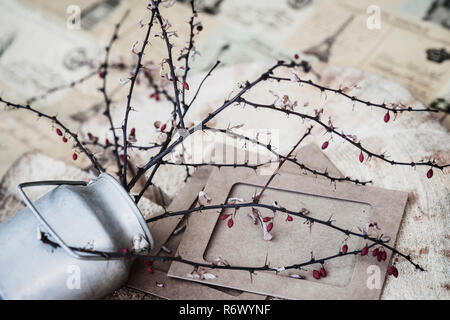 Style de vie encore décoratifs, de l'ikebana, le mensonge metal verseuse à branches épineuses à sec, les fruits rouges, les trames de papier sur fond de bois. Selective focus Banque D'Images