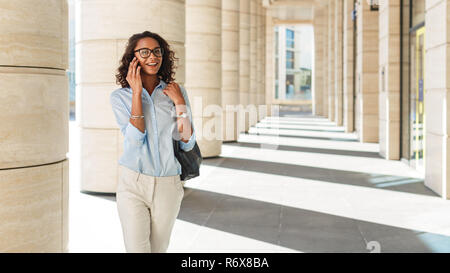 Smiling businesswoman walking outside office building et effectuer un appel téléphonique Banque D'Images